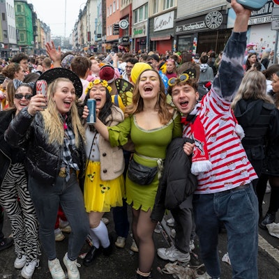 Eine Gruppe kostümierter Menschen feiert Karneval auf der Zülpicher Straße und lacht in die Kamera