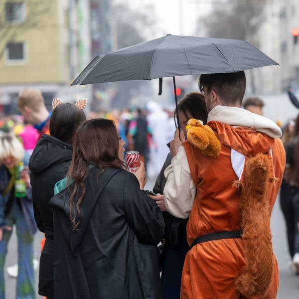 Feiernde im Kwartier Latäng stehen unter einem Regenschirm.