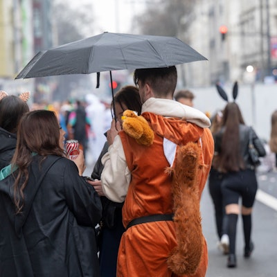 Feiernde im Kwartier Latäng stehen unter einem Regenschirm.