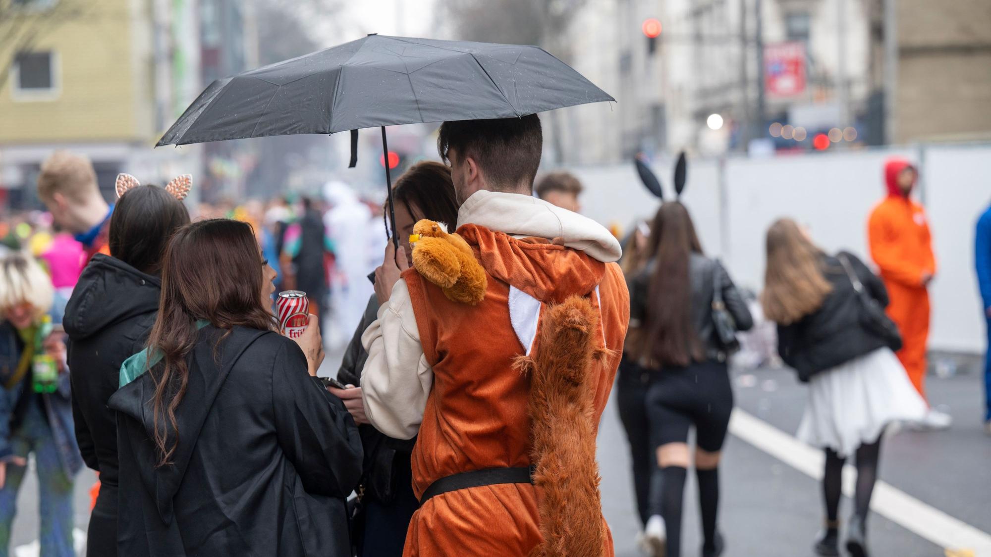 Feiernde im Kwartier Latäng stehen unter einem Regenschirm.