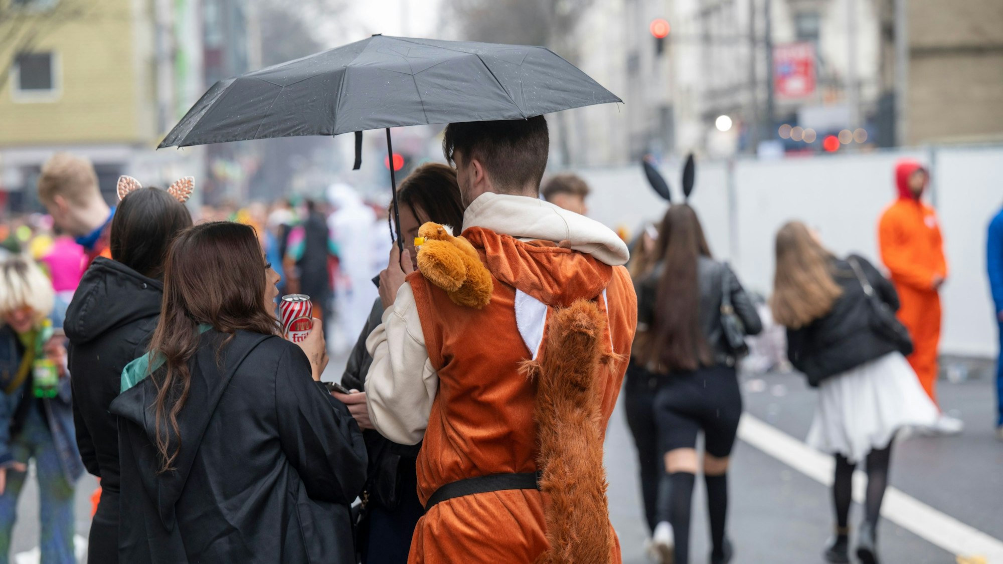 Feiernde im Kwartier Latäng stehen unter einem Regenschirm.
