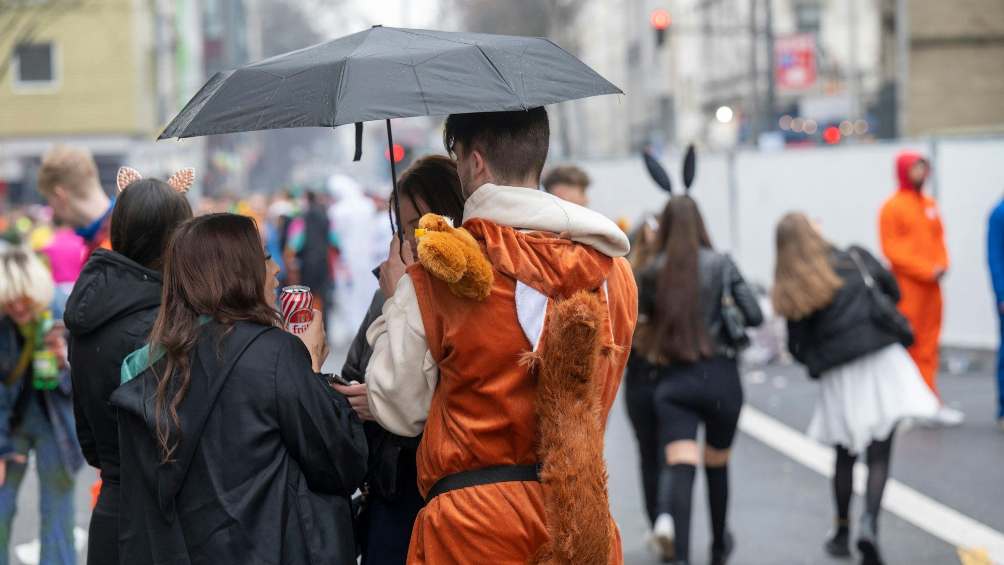 Ein Mann in einem Eichhörnchenkostüm und eine Frau im schwarzen Mantel stehen unter einem Regenschirm.