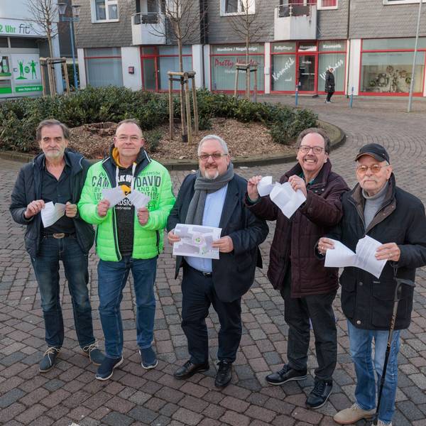 Auf der Straße „Am Marktplatz“ stehen fünf Männer und zerreißen symbolisch Papierdokumente.