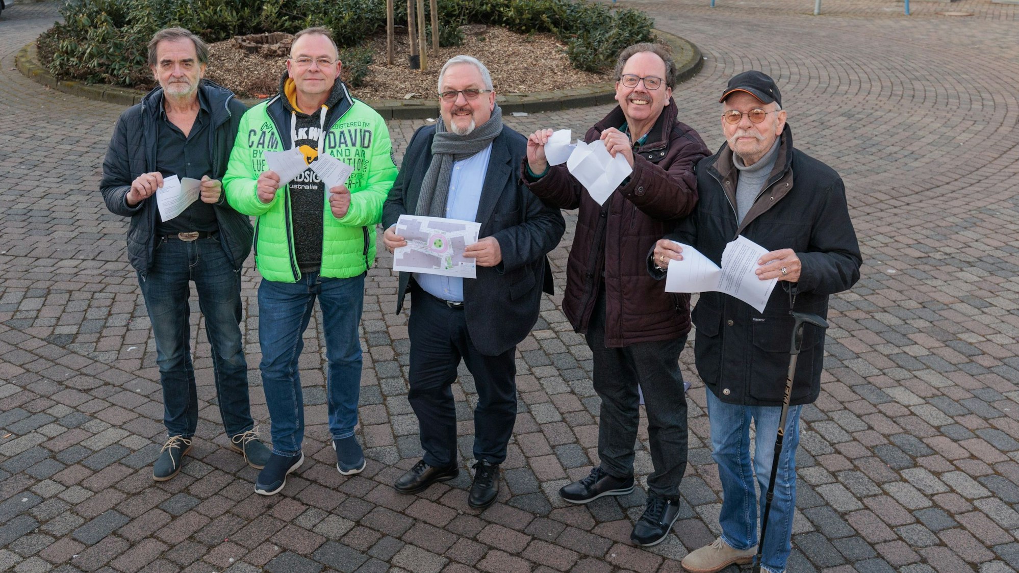 Auf der Straße „Am Marktplatz“ stehen fünf Männer und zerreißen symbolisch Papierdokumente.