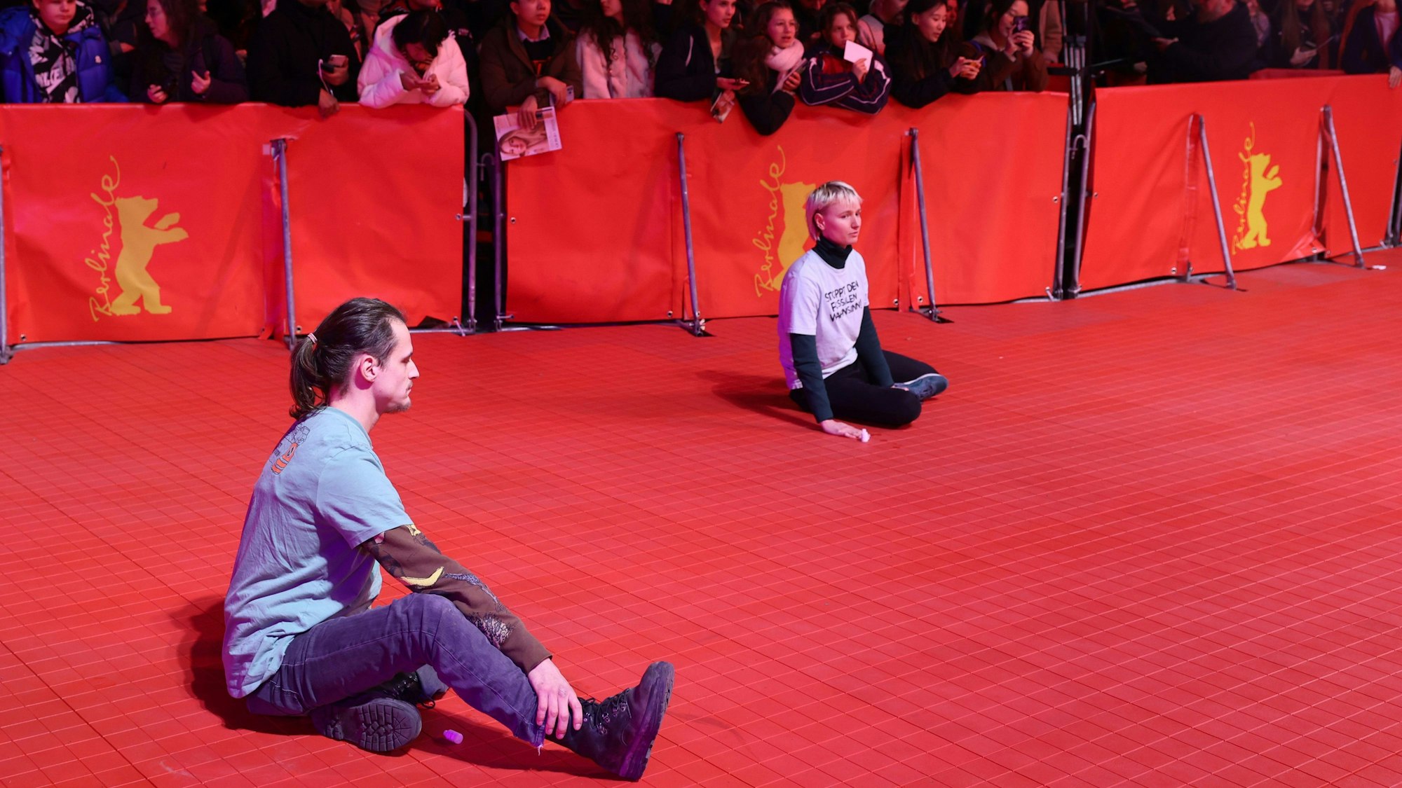 Zwei junge Menschen haben sich auf dem roten Teppich festgeklebt während der Eröffnung der Berlinale.