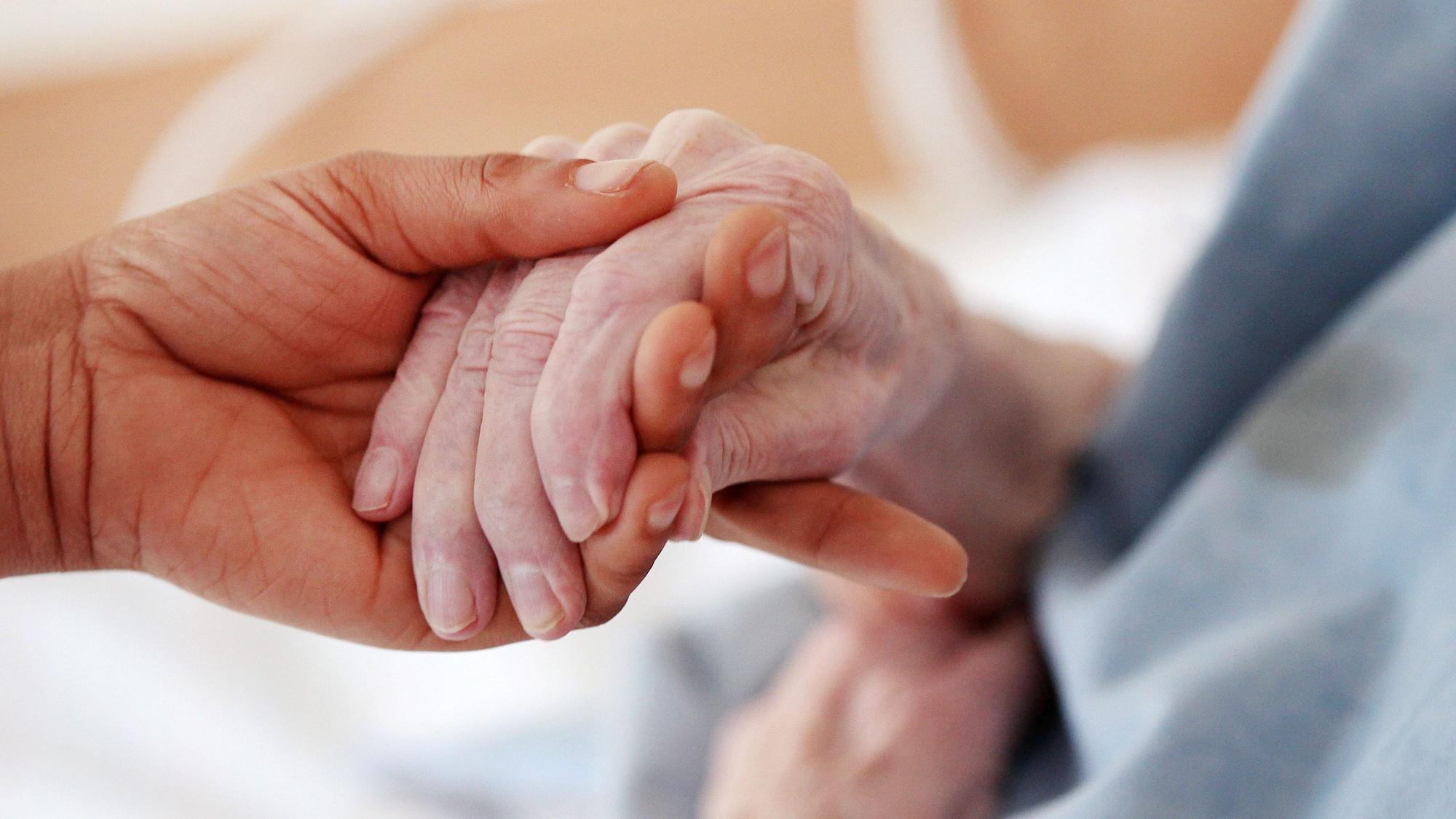 Eine Hand hält die Hand von einer älteren Person.