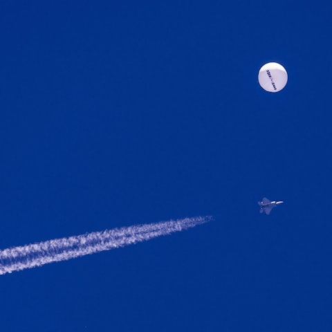 Ein F22-Kampfjet des US-Militärs fliegt in der Nähe des mutmaßlichen chinesischen Spionageballons. Beide sind deutlich am blauen Himmel zu sehen.