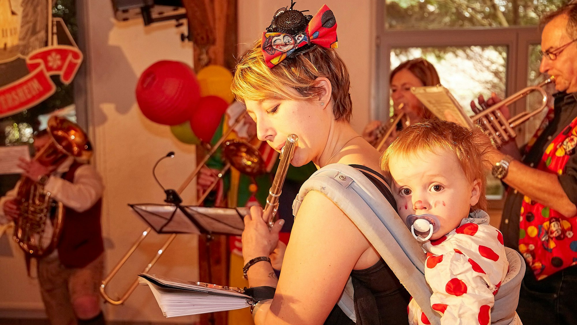 Eine Musikerin trägt ihr kleines Kind auf dem Rückem.