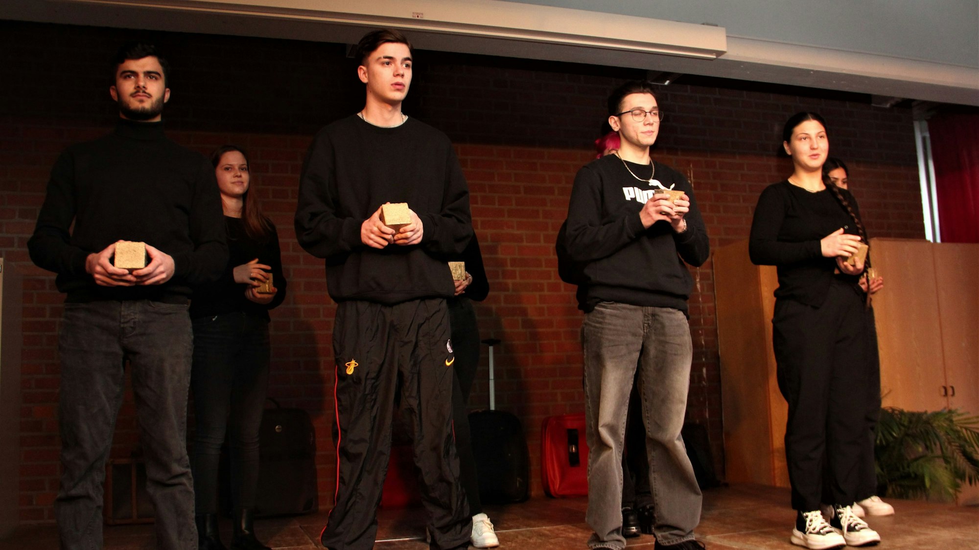Sechs junge Menschen stehen auf einer Bühne, sie halten Stolpersteine in der Hand.