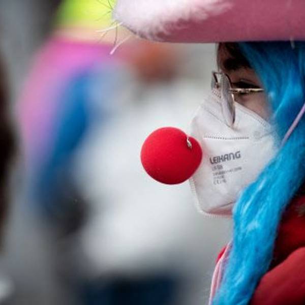 Eine verkleidete Frau trägt eine Clownsnase über einer FFP2 Maske.