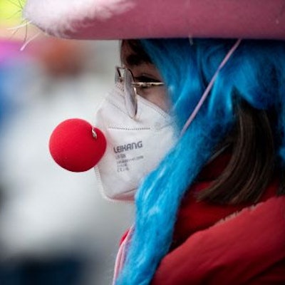 Eine verkleidete Frau trägt eine Clownsnase über einer FFP2 Maske.