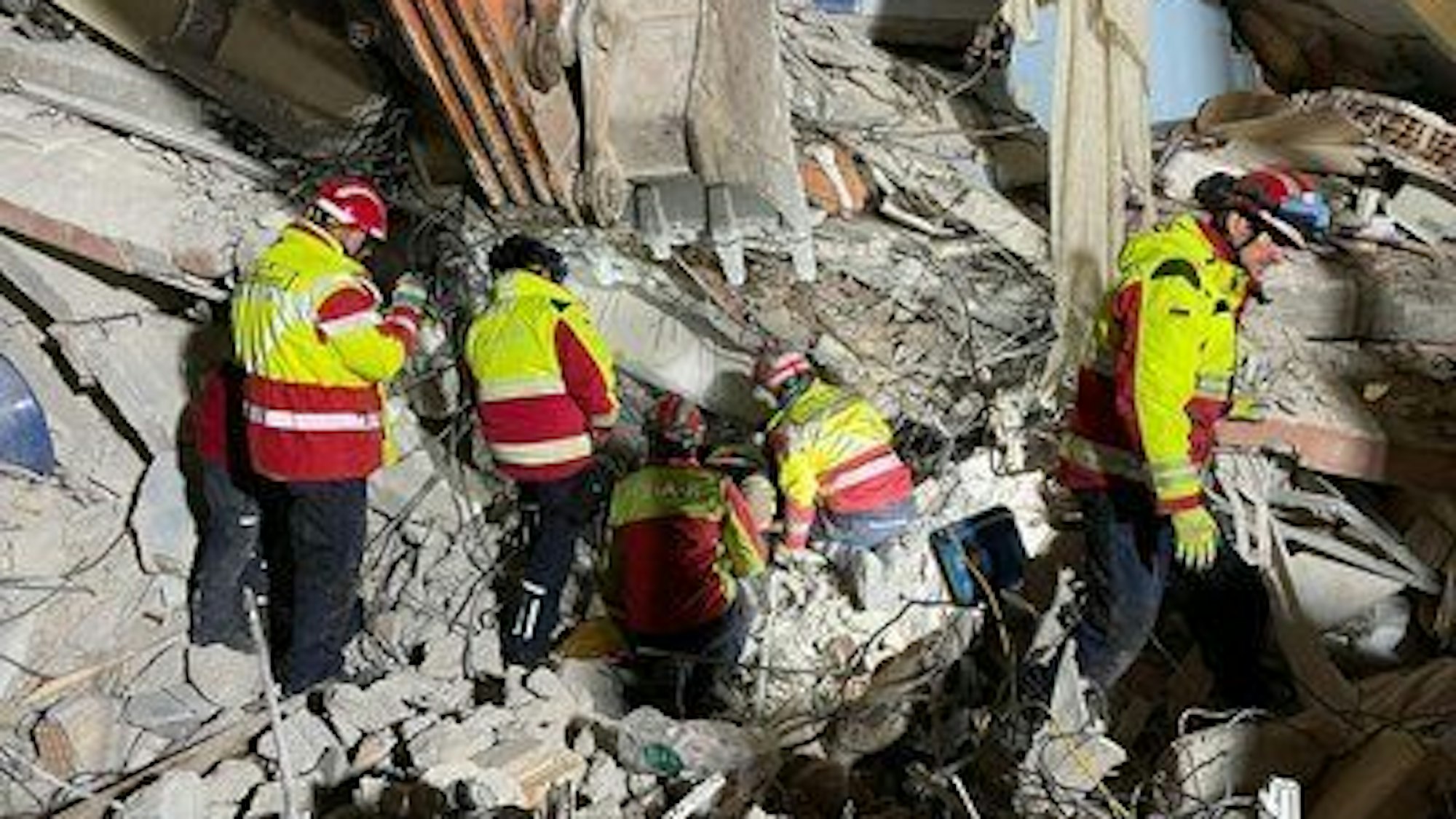 Fünf Retter in Warnanoraks suchen in Trümmern nach Überlebenden.