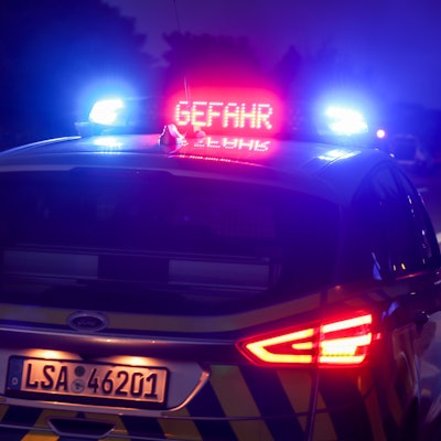 Ein Polizeiauto hat das Blaulicht an, außerdem ist in roten Buchstaben „Gefahr“ auf dem Dach des Einsatzwagens zu lesen. Im Hintergrund ist eine Unfallstelle zu sehen. (Symbolbild)