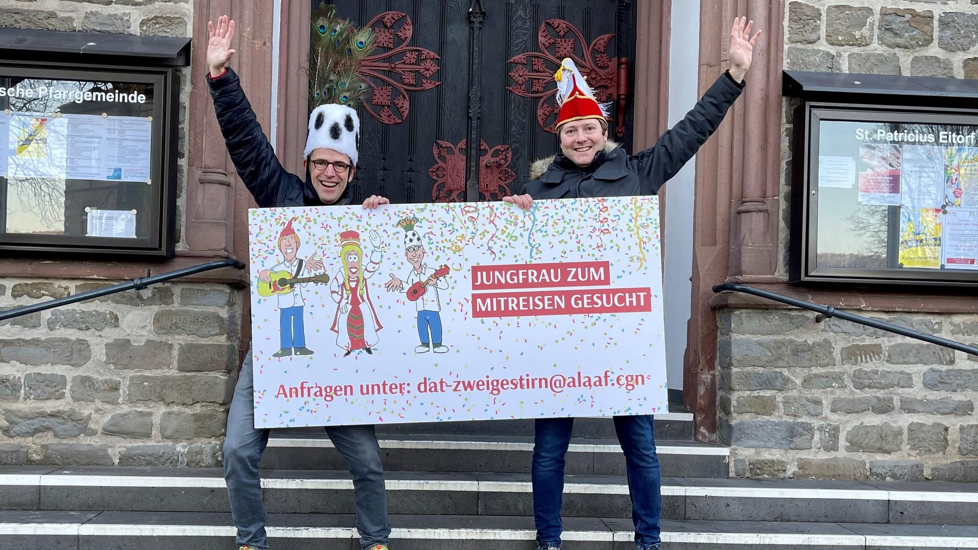 Es sind die beiden Männer zu sehen, die ein Schild mit der Aufschrift „Jungfrau zum mitreisen gesucht“ hochhalten.