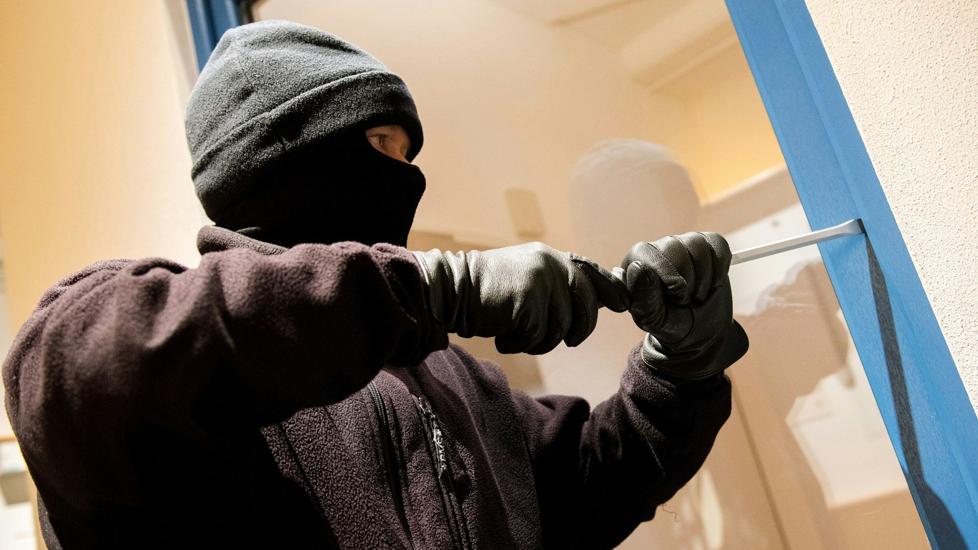 Ein als Einbrecher verkleideter Mann hebelt in der Kriminalpolizeilichen Beratungsstelle der Polizei ein Fenster auf.