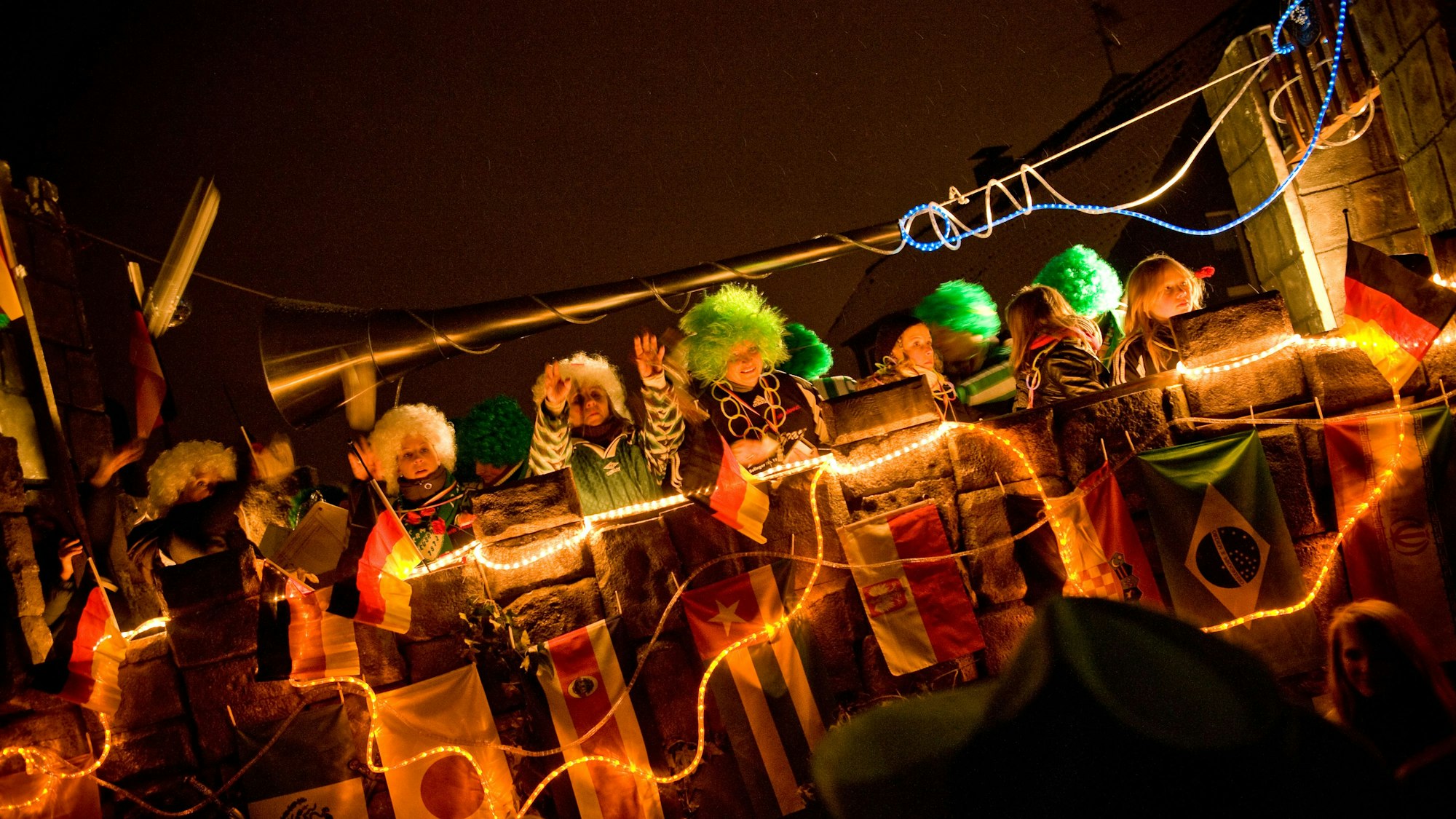 Beleuchteter Festwagen mit verkleideten Jecken beim Zug in der Dunkelheit.