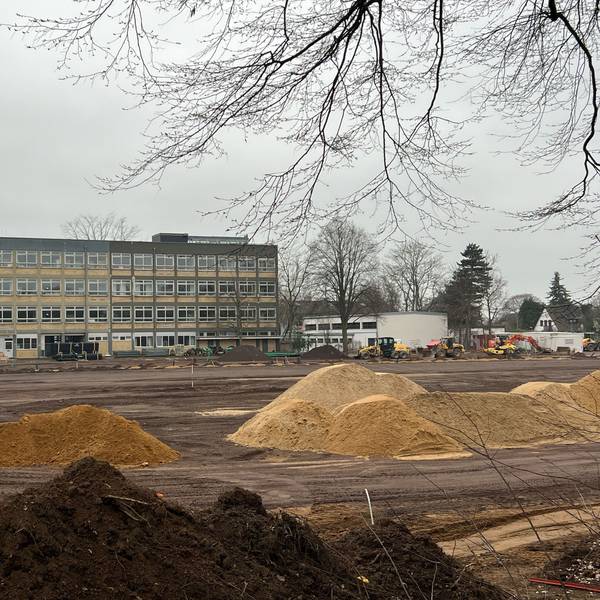 Das Bild zeigt aufgeschüttete Sandhaufen und Baugerät vor dem Gymnasium.