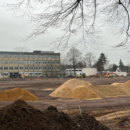 Das Bild zeigt aufgeschüttete Sandhaufen und Baugerät vor dem Gymnasium.
