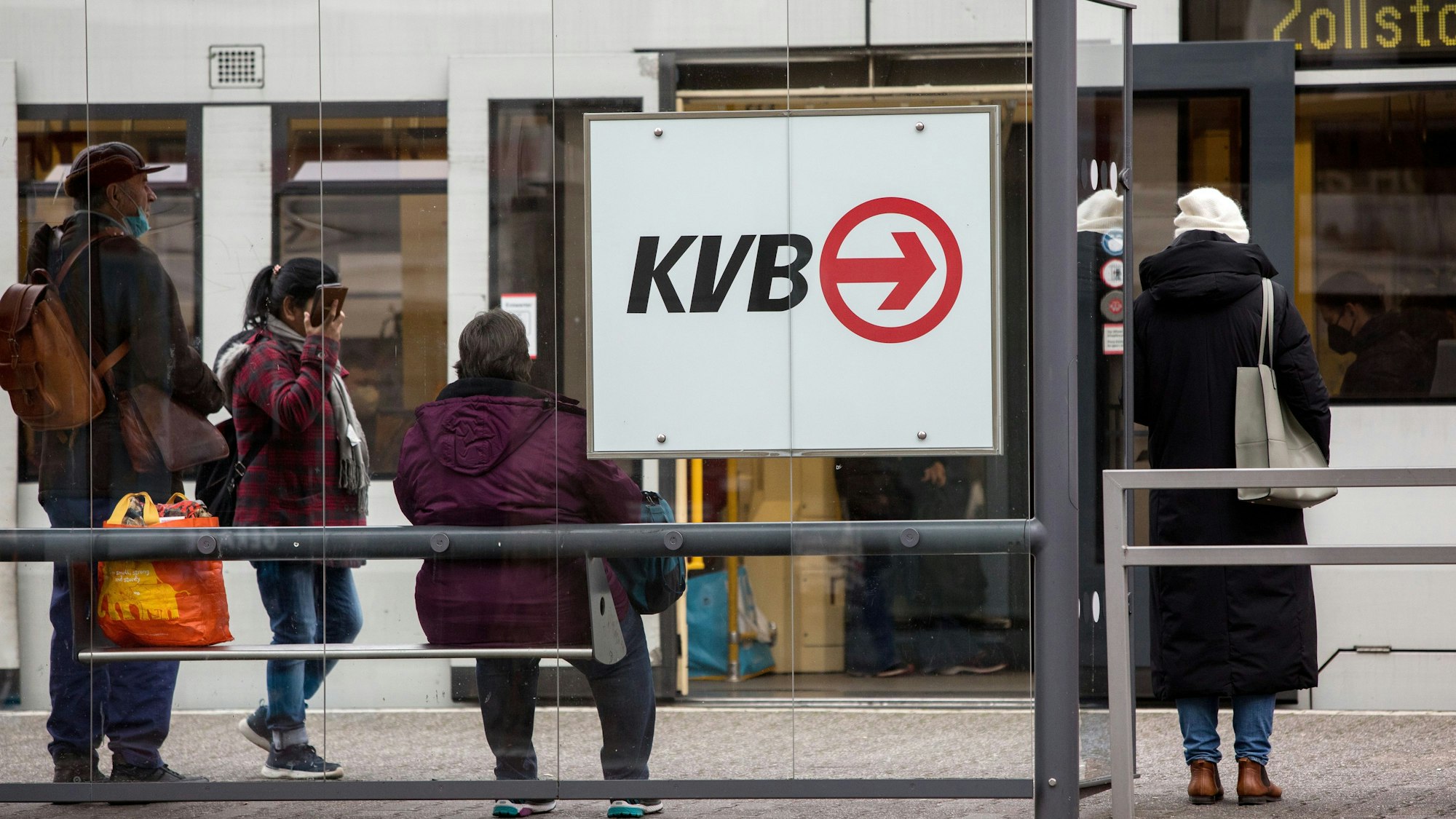 Menschen an der Haltestelle Barbarossaplatz. Im Hintergrund eine Bahn der Linie 12 in Richtung Zollstock (Symbolbild)