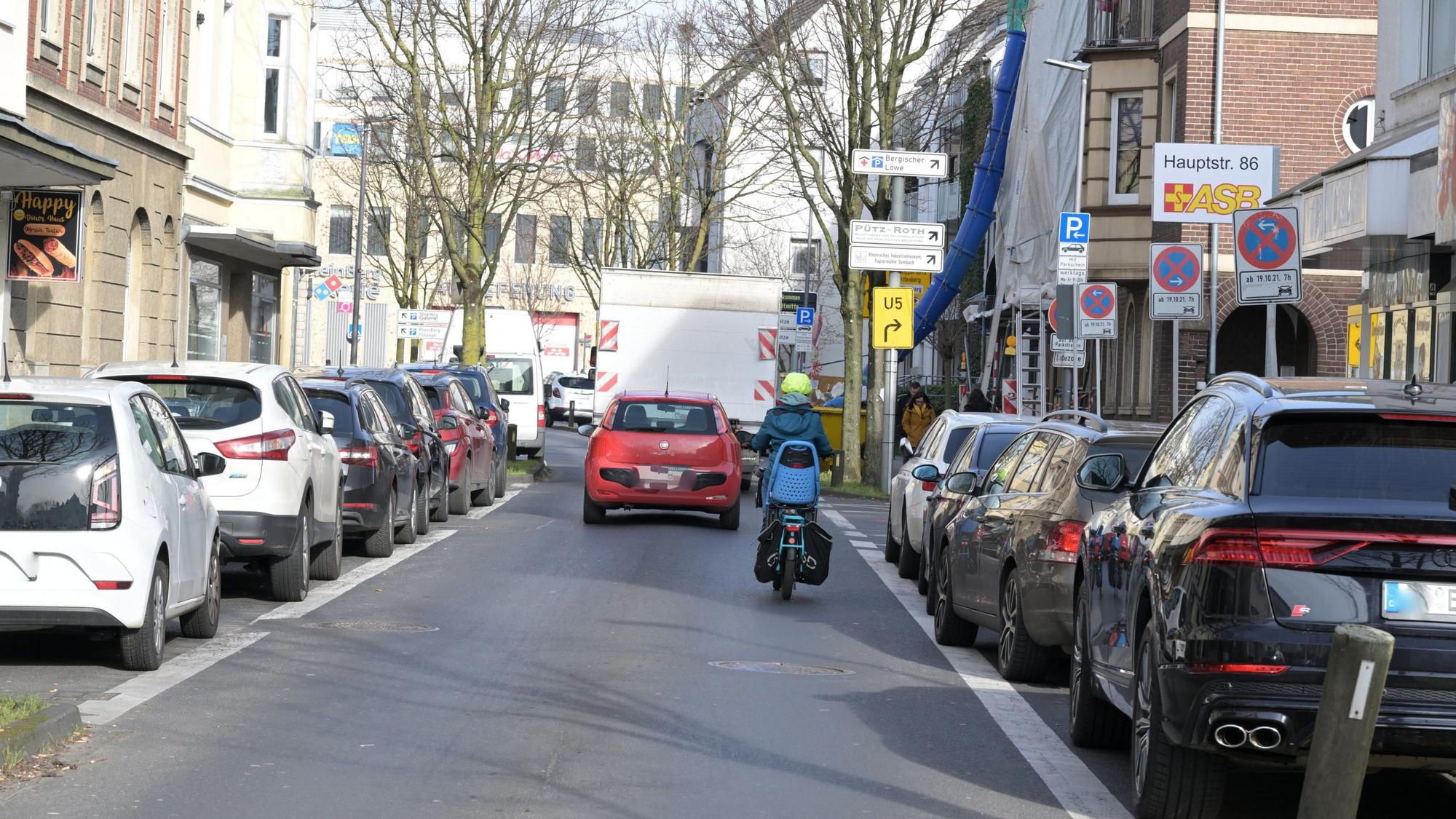 Ein Radfahrer fährt auf der Fahrbahn der unteren Hauptstraße. vor ihm fährt ein rotes Auto.