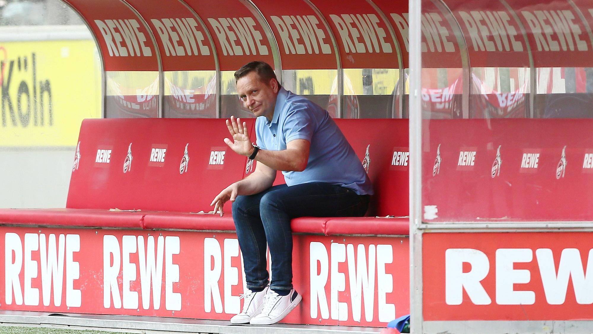 Horst Heldt sitzt auf einer Bank, die mit „Rewe“ plakatiert ist.
