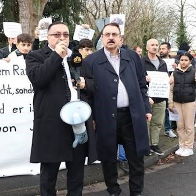 Mehrere Demonstrierende stehen hinter dem Redner und halten Schilder.