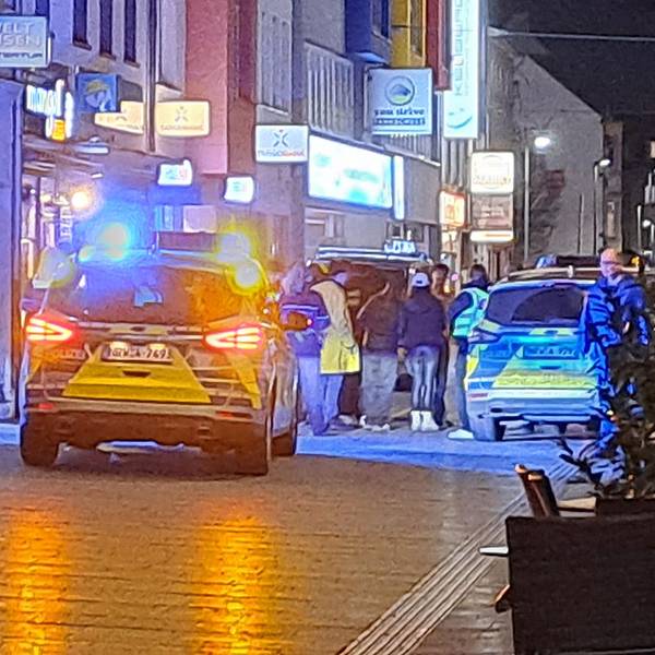 Zwei Streifenwagen stehen mit Blaulicht in der Bergisch Gladbacher Fußgängerzone. Polizeibeamte stehen bei einer Ansammlung von Menschen.
