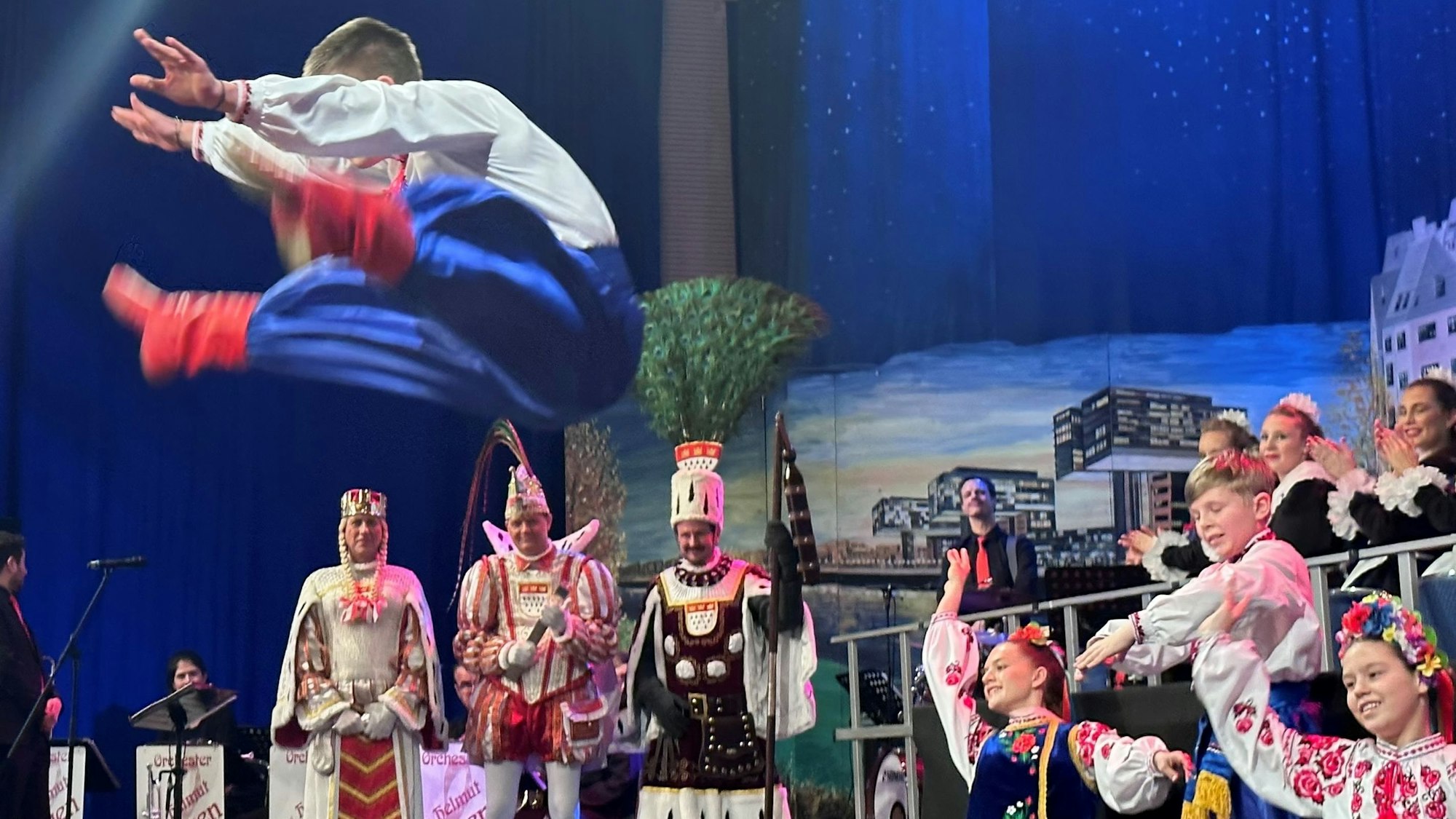 Kinder tanzen vor dem Dreigestirn vor blauem Bühnenhintergrund