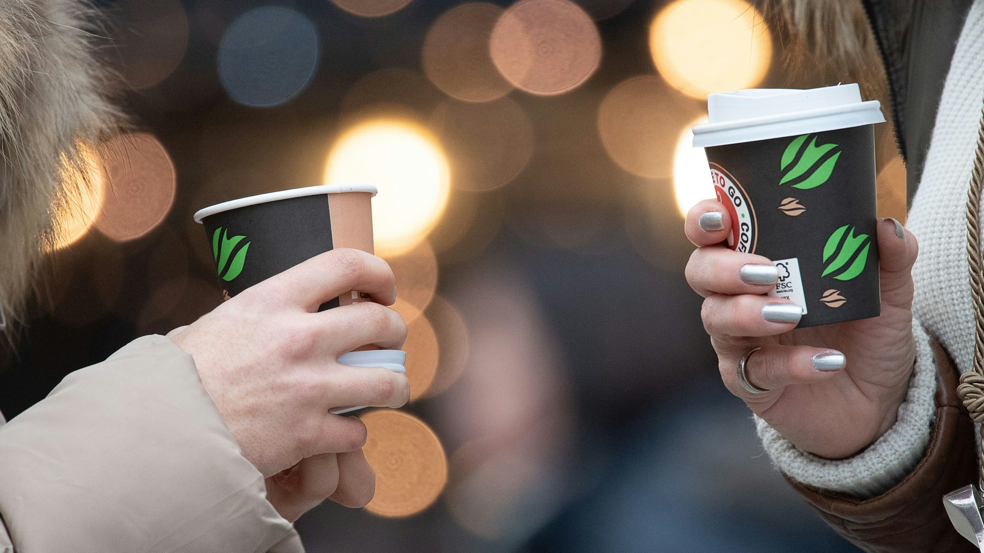 Zwei Frauen trinken einen Kaffee in der Innenstadt aus Coffee-to-go-Bechern. Der rechte Becher hat einen Deckel, der linke nicht. (Symbolbild)