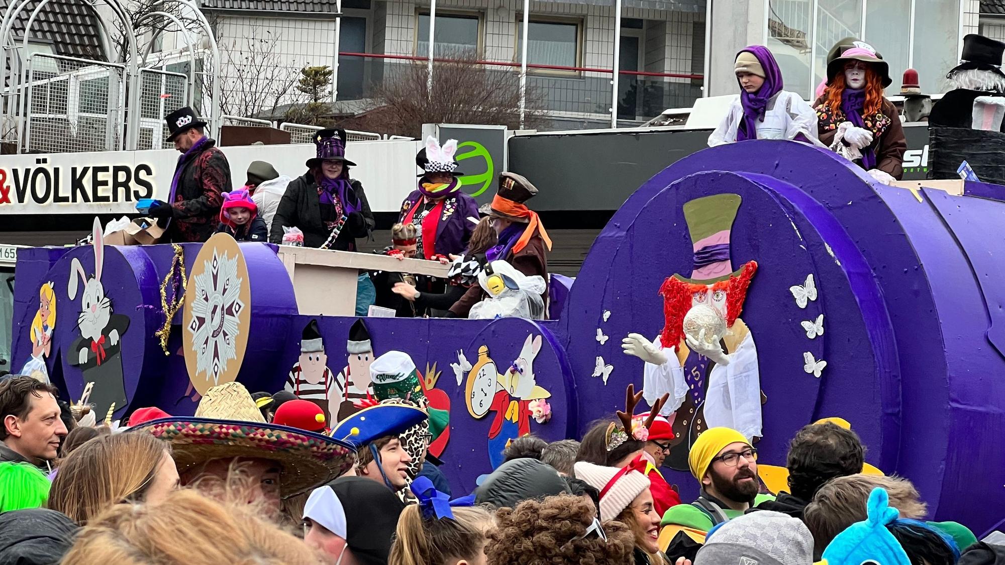 Der lila angestrichene Festwagen der KG Herrenelferrat mit Figuren aus Alice im Wunderland im Blütensamstagszug