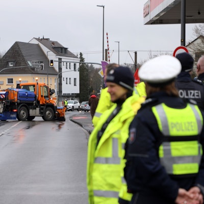 Polizisten stehen auf einer Straße, ein Streufahrzeug blockiert die Fahrbahnen.