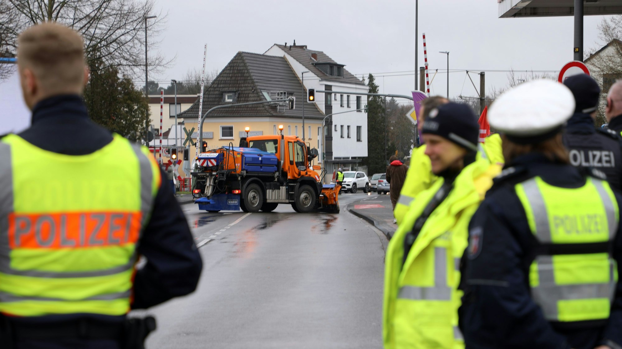 Polizisten stehen auf einer Straße, ein Streufahrzeug blockiert die Fahrbahnen.