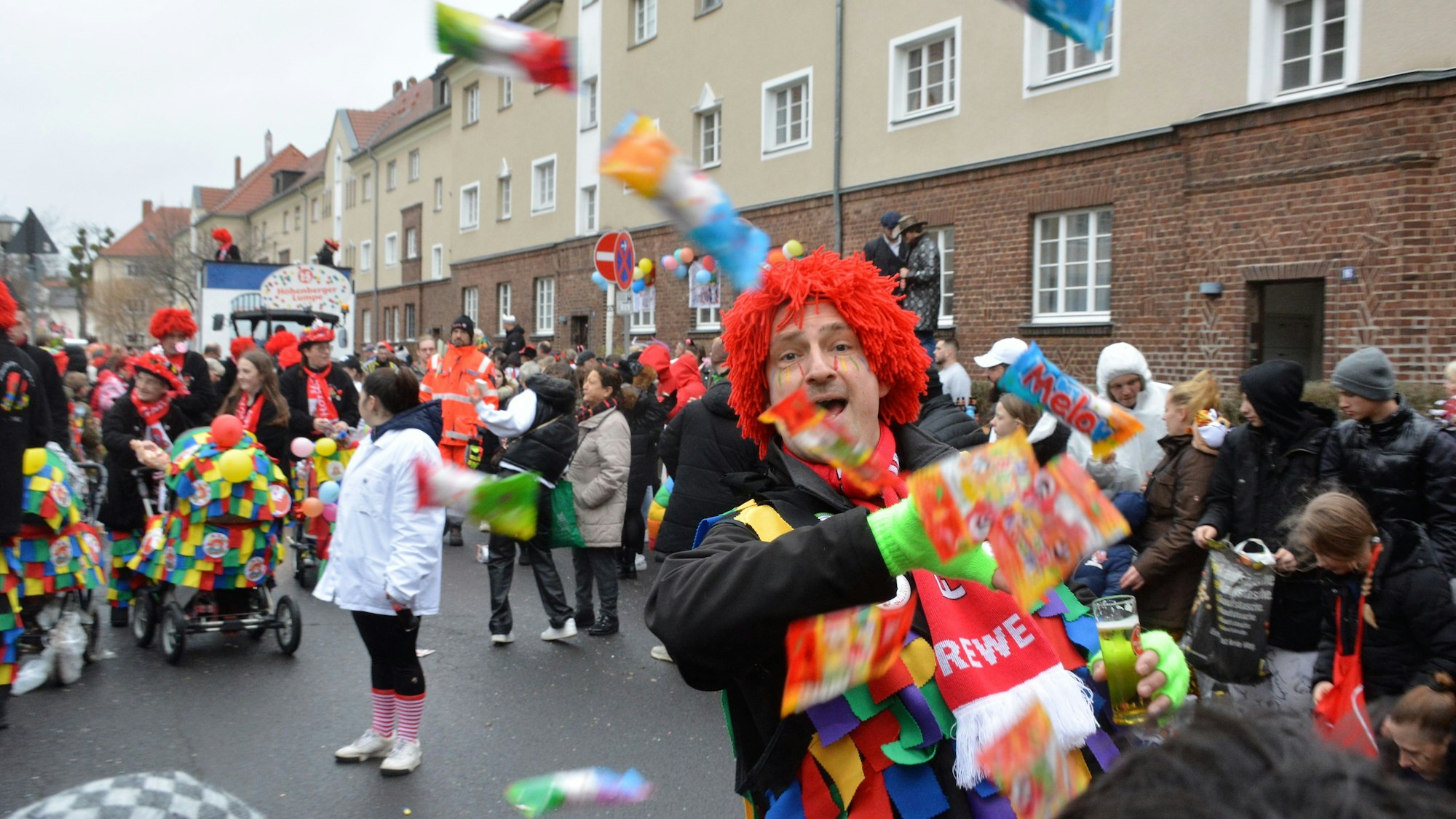 Ein Mann im Clownskostüm wirft Kamelle in die Luft.