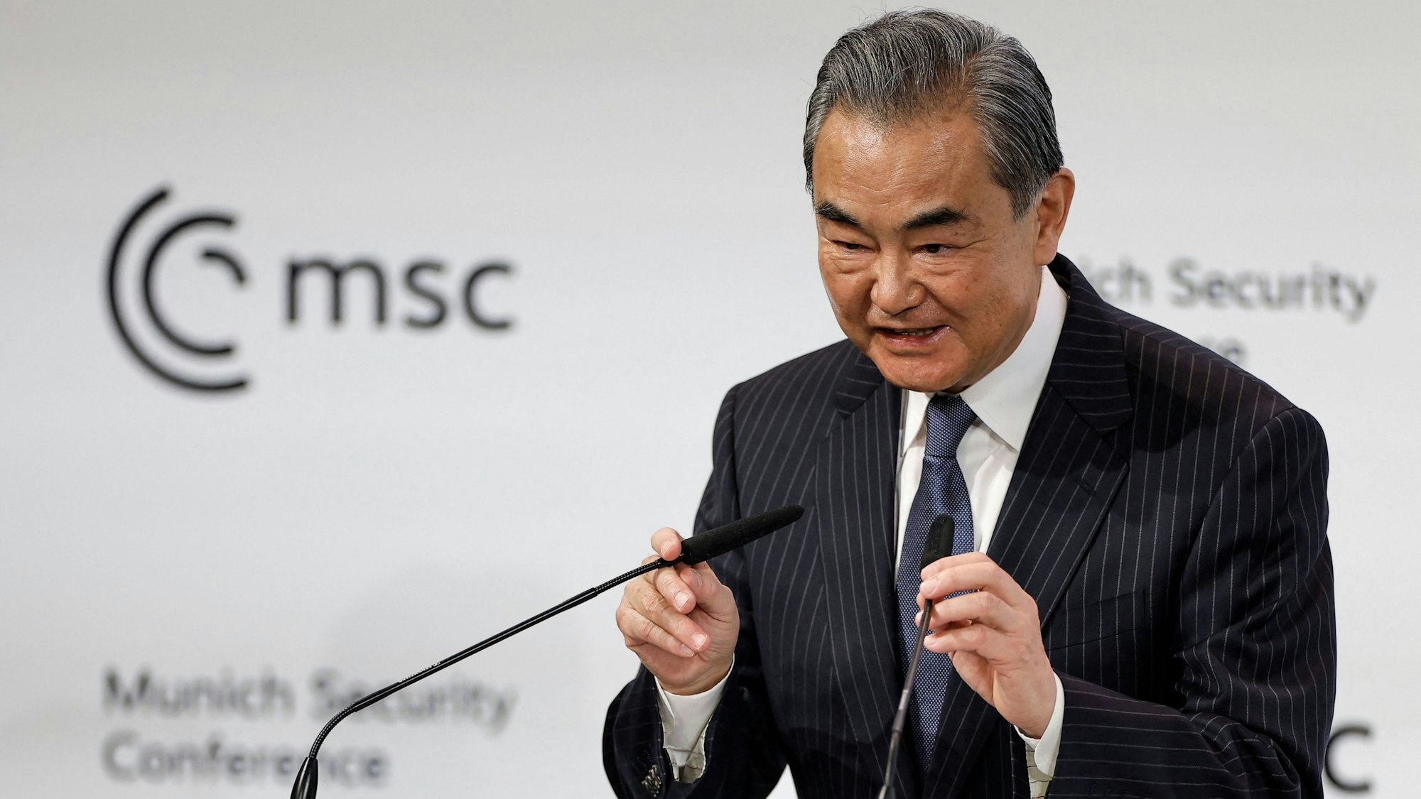 Der oberste chinesische Außenpolitiker Wang Yi spricht auf der Münchener Sicherheitskonferenz und richtetet die Mikrophone zu seinem Gesicht.
