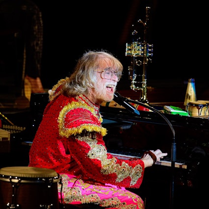 Schneider in Torero-Kleidung am Flügel. Auf diesem stehen unter Anderem eine Trompete und Rasseln.