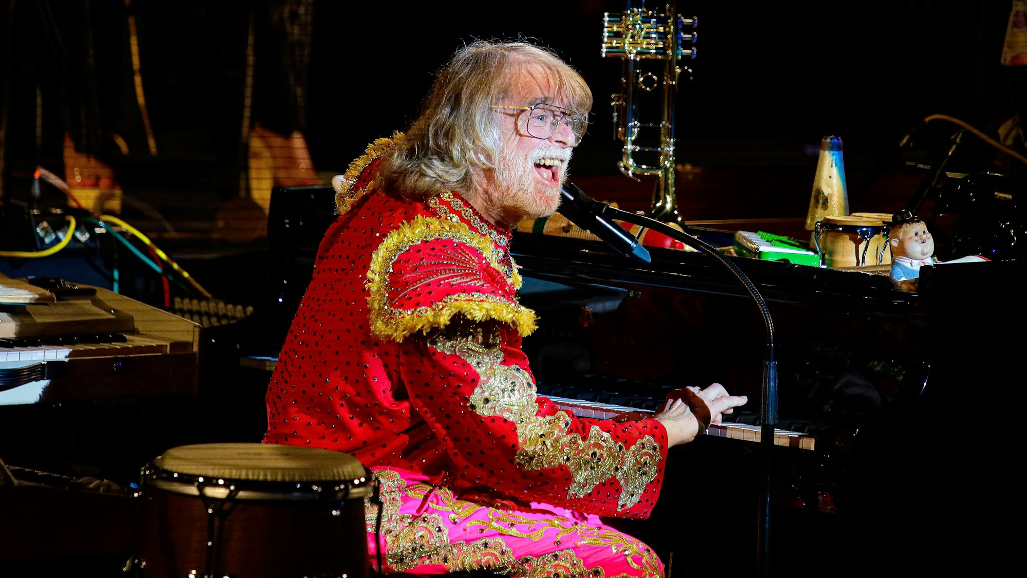 Schneider in Torero-Kleidung am Flügel. Auf diesem stehen unter Anderem eine Trompete und Rasseln.