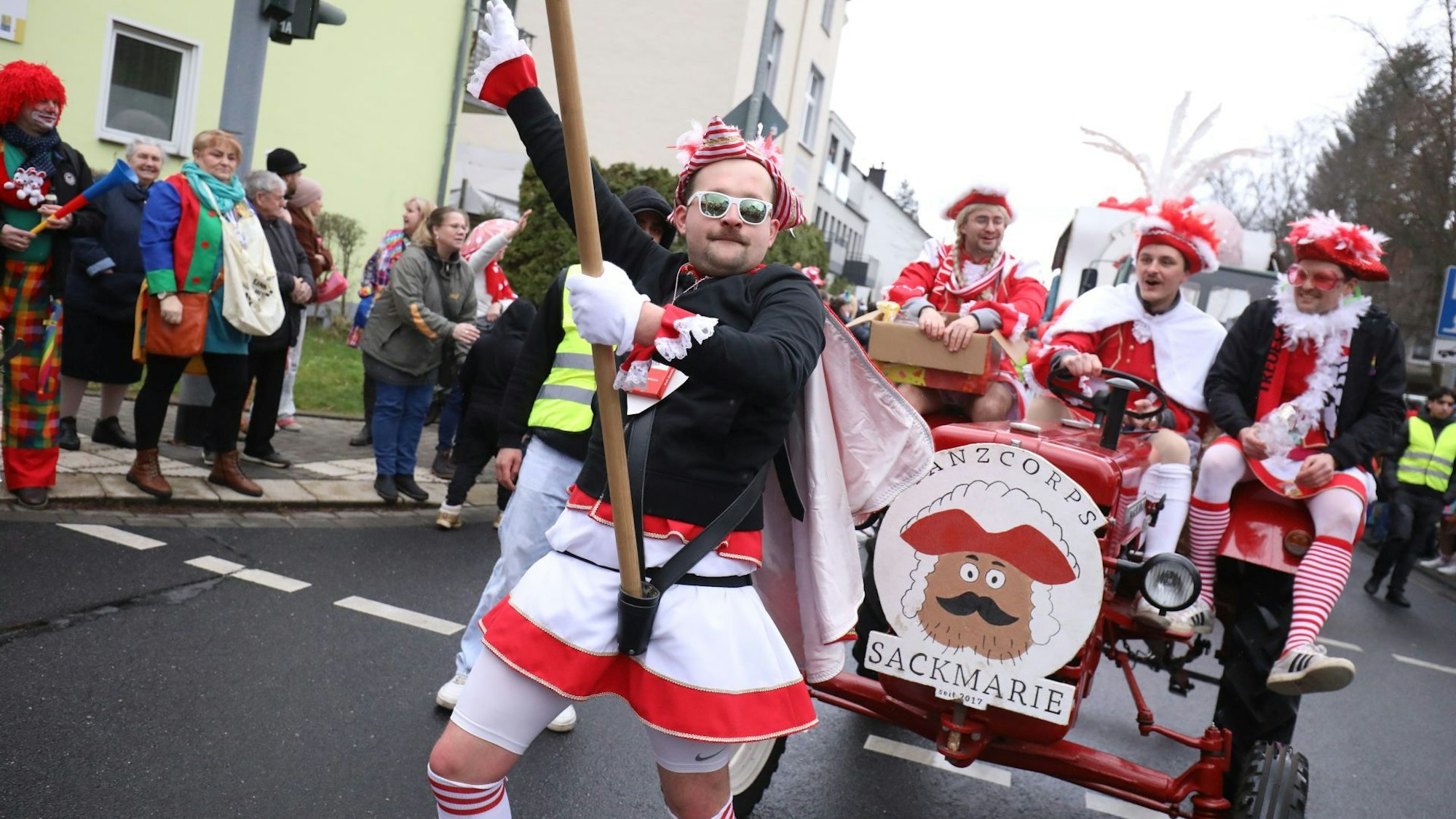 Rot-weiß gekleidete Männer des Tanzcorps Sackmarie fahren auf einem roten Wagen im Siebengebirgszug mit.