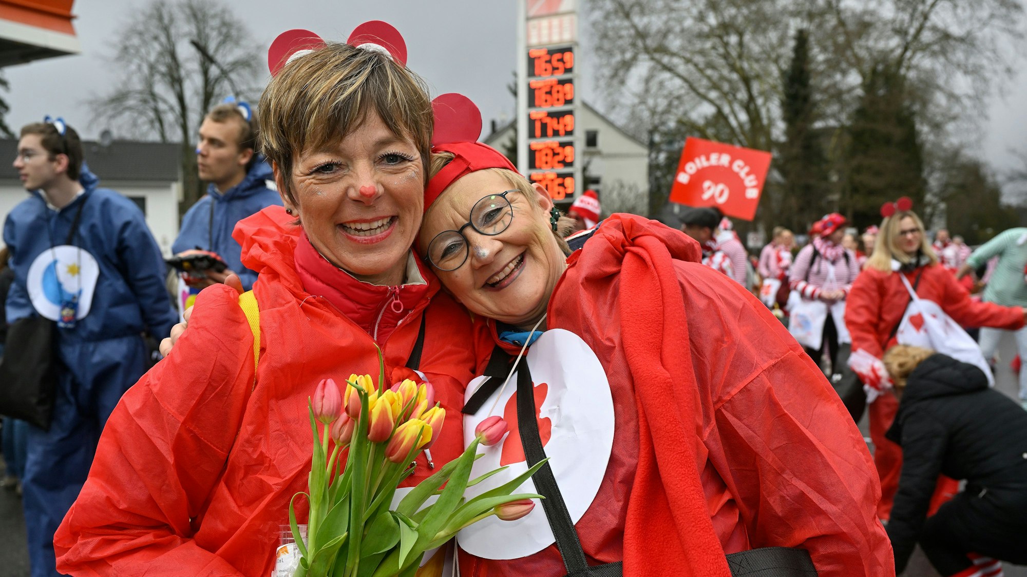 Zwei rot verkleidete Frauen lächeln Arm in Arm in die Kamera.