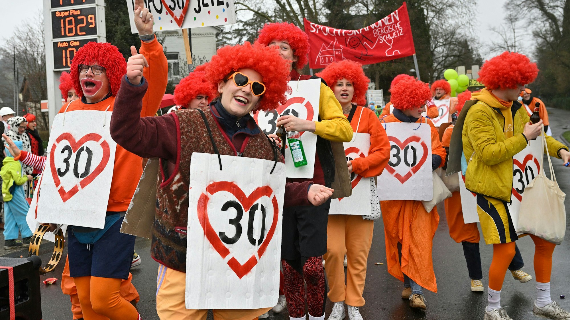 Jecke tragen rote Perücken und Schilder mit der Zahl 30 sowie roten Herzen darum drauf.