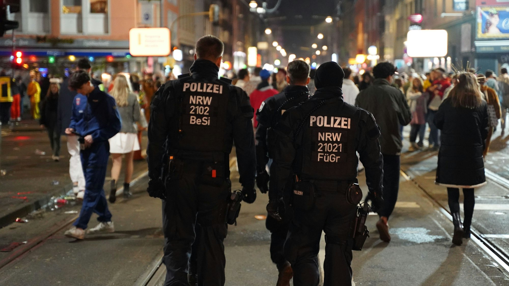 Zwei Polizisten gehen in Uniform über die Zülpicher Straße. Im Hintergrund sind zahlreiche Menschen zu erkennen, die Karneval feiern.