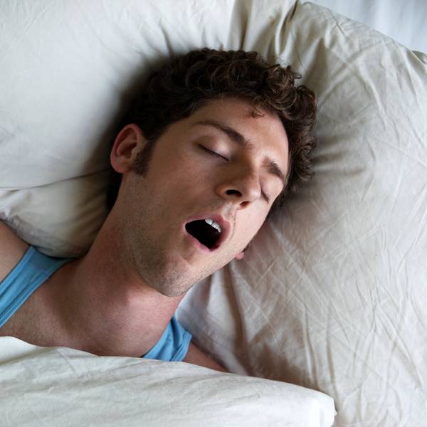 Mann liegt im Bett und schnarcht mit offenem Mund.