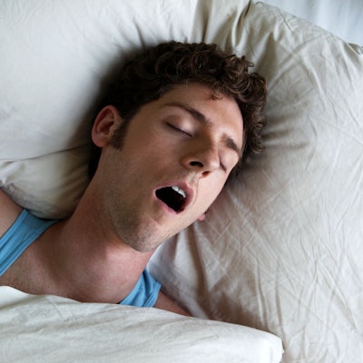 Mann liegt im Bett und schnarcht mit offenem Mund.