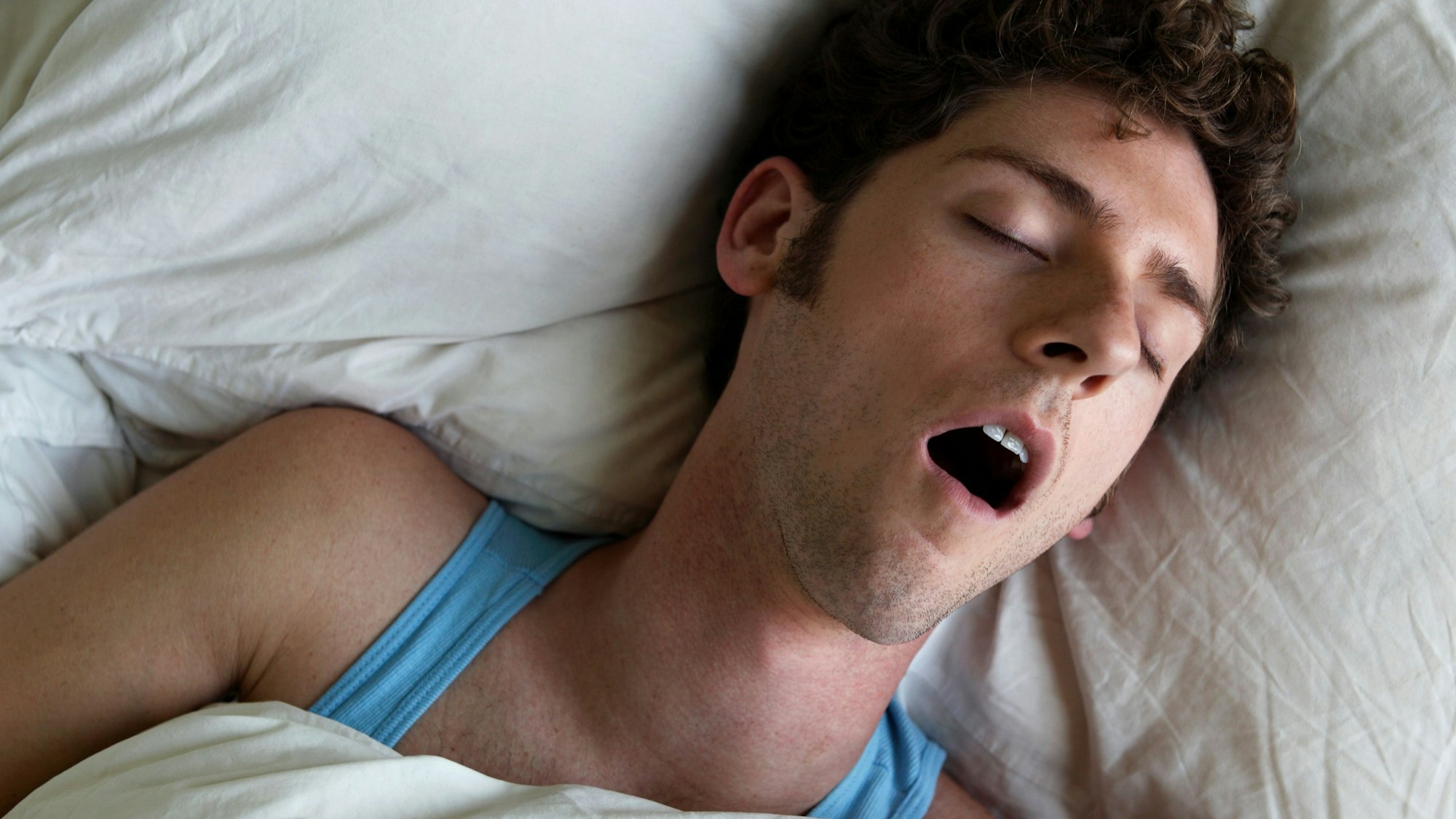 Mann liegt im Bett und schnarcht mit offenem Mund.