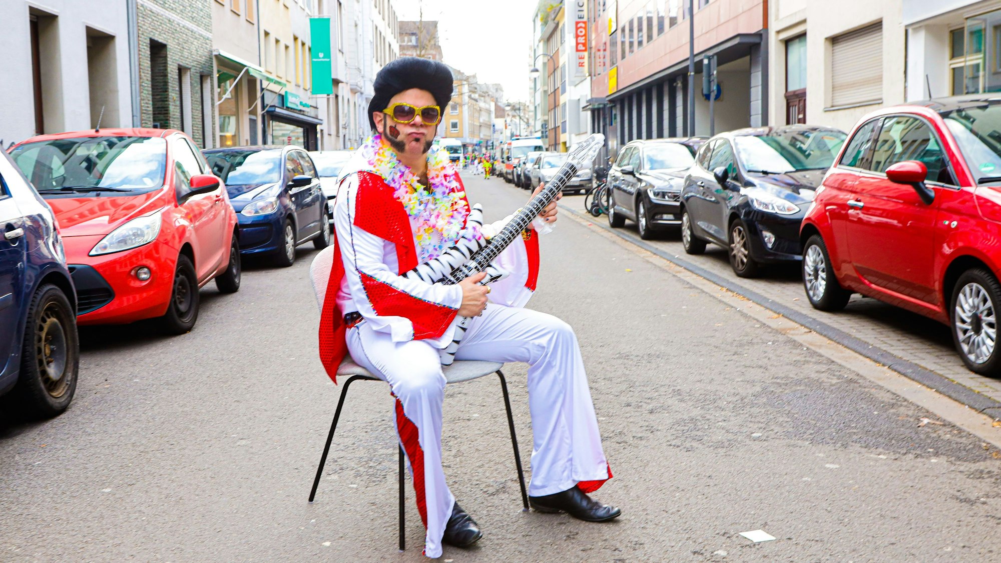 Die Mohrenstraße in Köln am Rosenmontag.Tobias Oentrup, verkleidet als Elvis Presley, sitzt auf einem Stuhl mitten auf der Straße