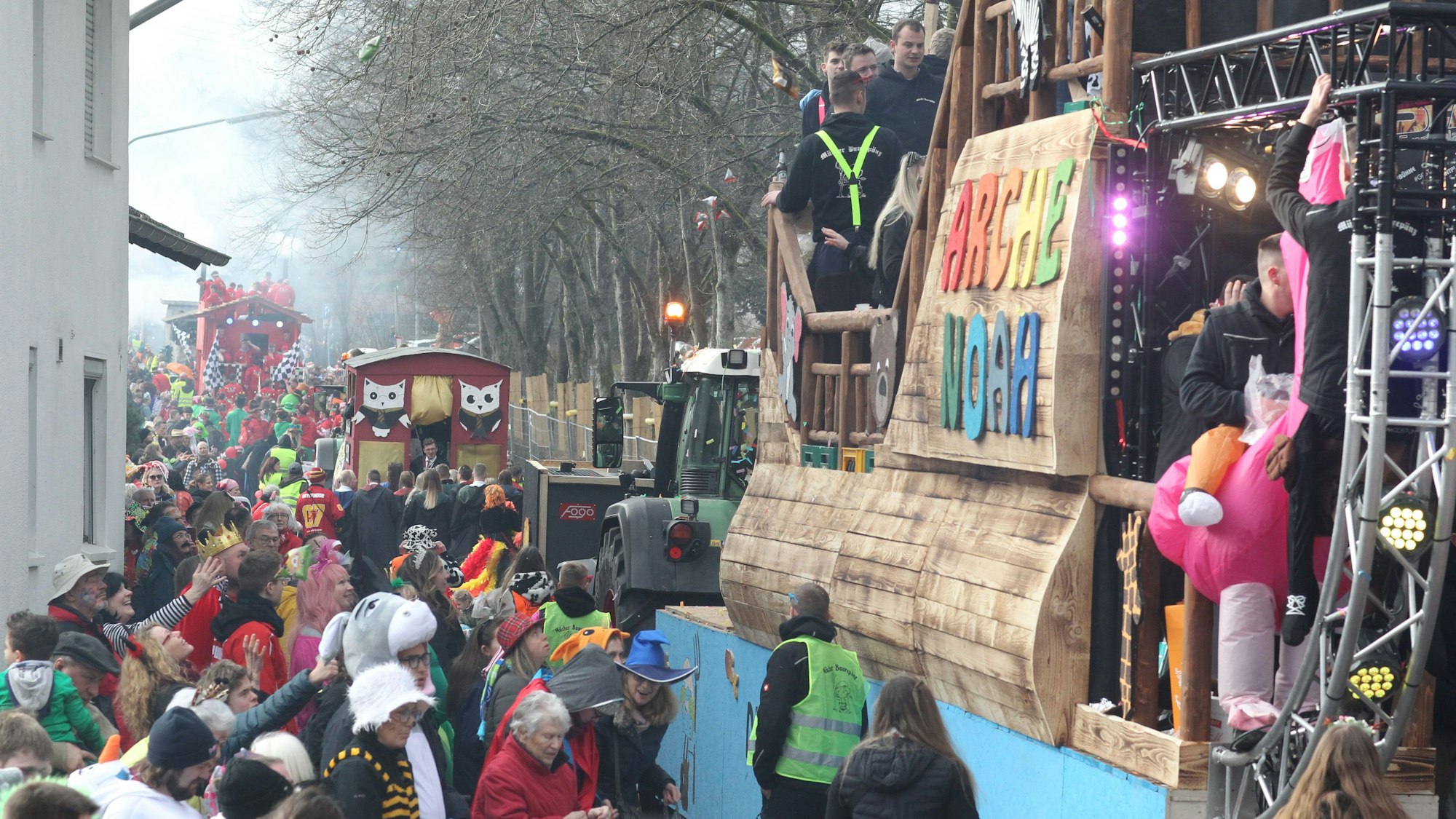 Ein Karnevalswagen fährt begleitet von vielen Menschen durch eine Straße.