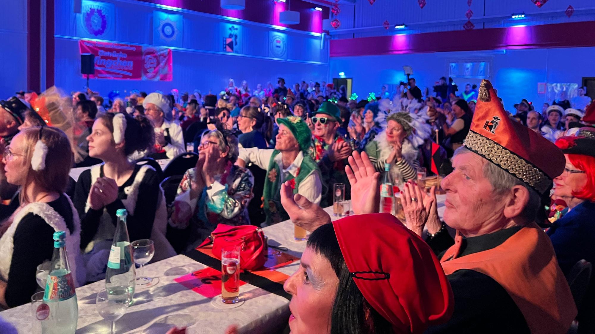 Voll besetzte Festhalle mit applaudierenden und verkleideten Karnevalistinnen und Karnevalisten.
