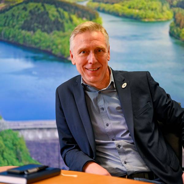 Dr. Uwe Moshage sitzt vor einer großen Luftaufnahme der Aggertalsperre.