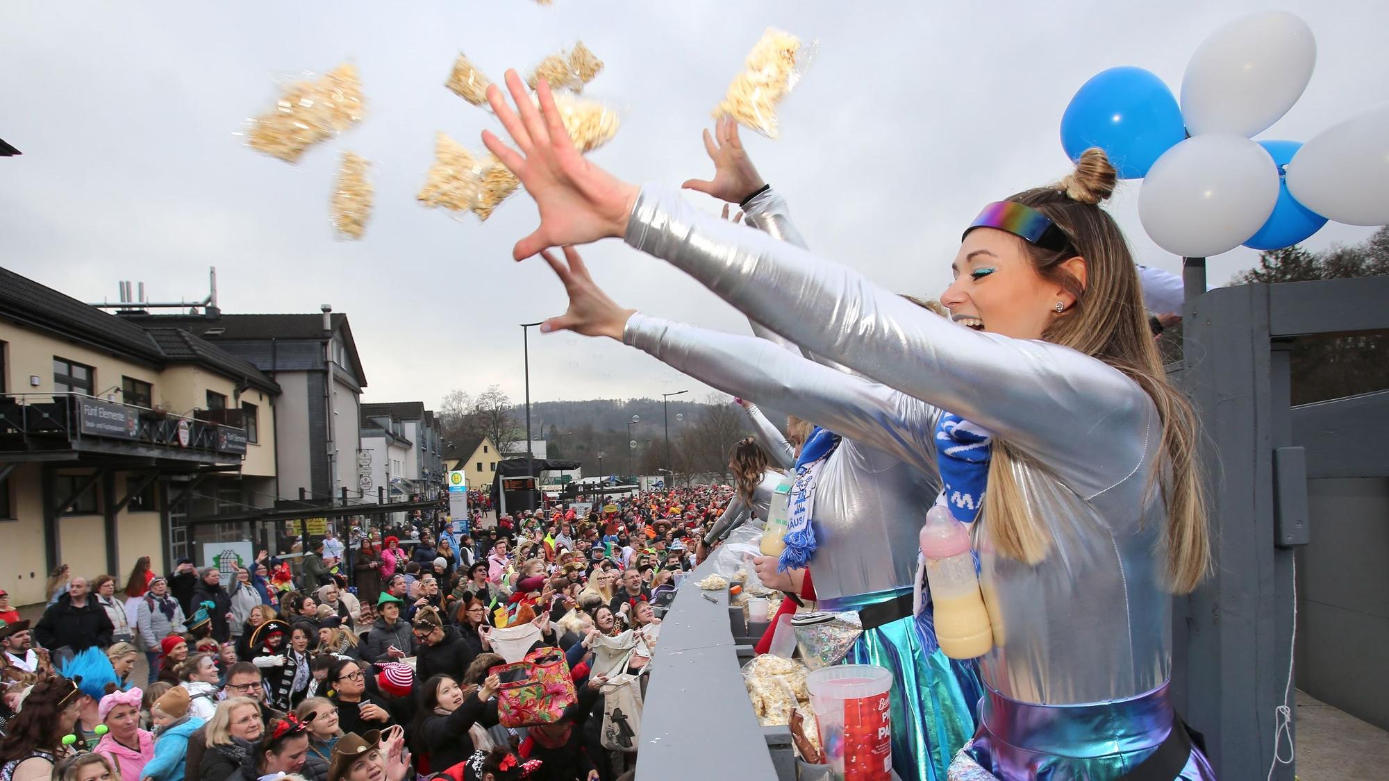 Fröhliche Jeckinnen werfen Popcorn-Tüten von einem Wagen in die Menschenmenge.