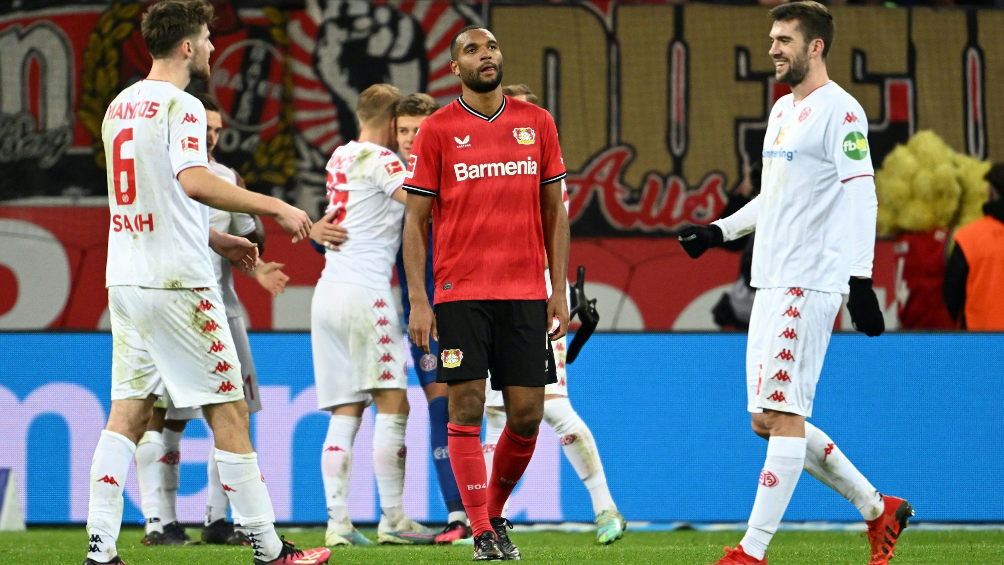 19.02.2023, Nordrhein-Westfalen, Leverkusen: Fußball: Bundesliga, Bayer Leverkusen - FSV Mainz 05, 21. Spieltag, in der BayArena: Leverkusens Jonathan Tah (M) steht nach dem Spiel auf dem Platz, während die Mainzer ihren 2:3-Auswärtssieg feiern. Foto: Federico Gambarini/dpa - WICHTIGER HINWEIS: Gemäß den Vorgaben der DFL Deutsche Fußball Liga bzw. des DFB Deutscher Fußball-Bund ist es untersagt, in dem Stadion und/oder vom Spiel angefertigte Fotoaufnahmen in Form von Sequenzbildern und/oder videoähnlichen Fotostrecken zu verwerten bzw. verwerten zu lassen. +++ dpa-Bildfunk +++