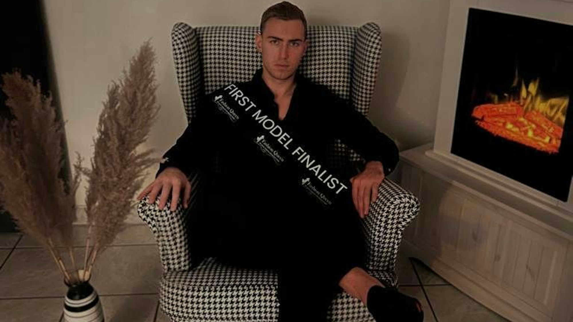 Dennis aus Erftstadt sitzt in einem Sessel, er trägt eine Schärpe mit der Aufschrift „First Model Finalist“.